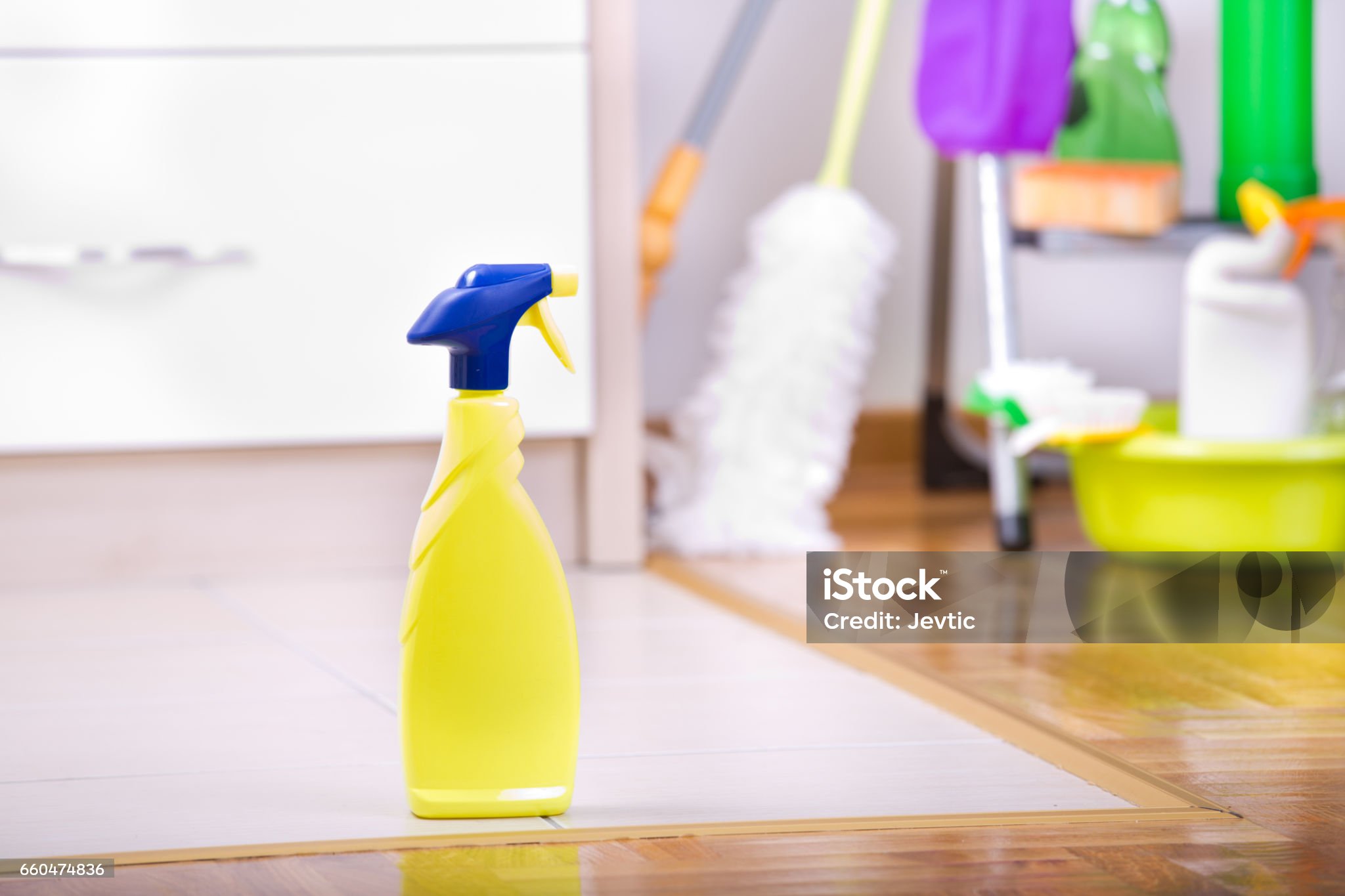 Close up of spray bottle for floor cleaning on the ceramic tiles and different cleaning supplies and equipment in background